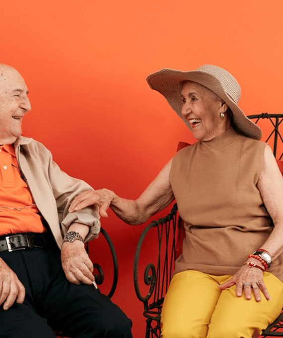 Couple sitting in chairs laughing against an orange background
