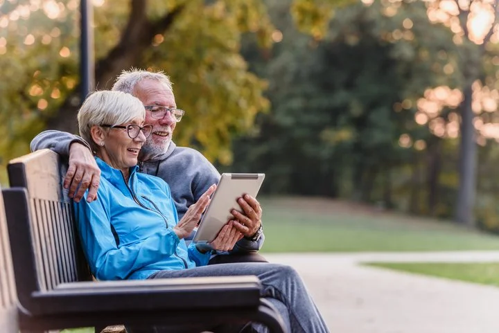 Pareja sentada en un banco del parque utilizando una tableta digital.