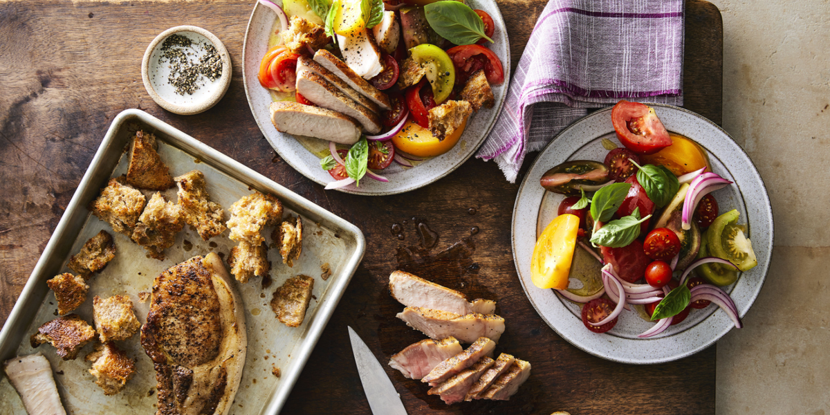 Roasted pork chops with marinated tomatoes and croutons plated on a table with a napkin