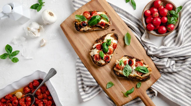 Chicken melt garnished with basil and tomatoes placed on a wooden slate.
