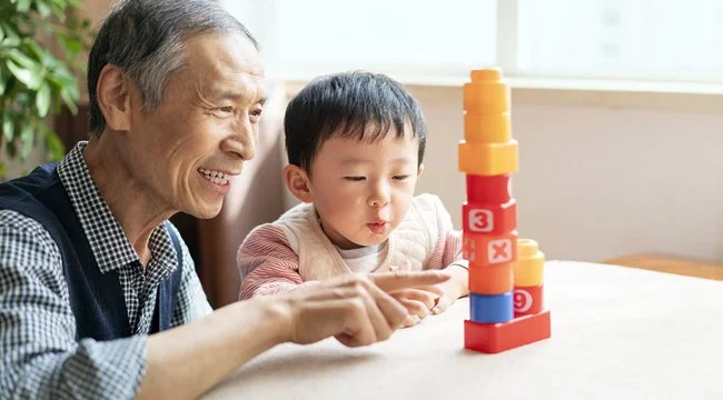 Grandfather and grandchild sitting at a table and playing with blocks